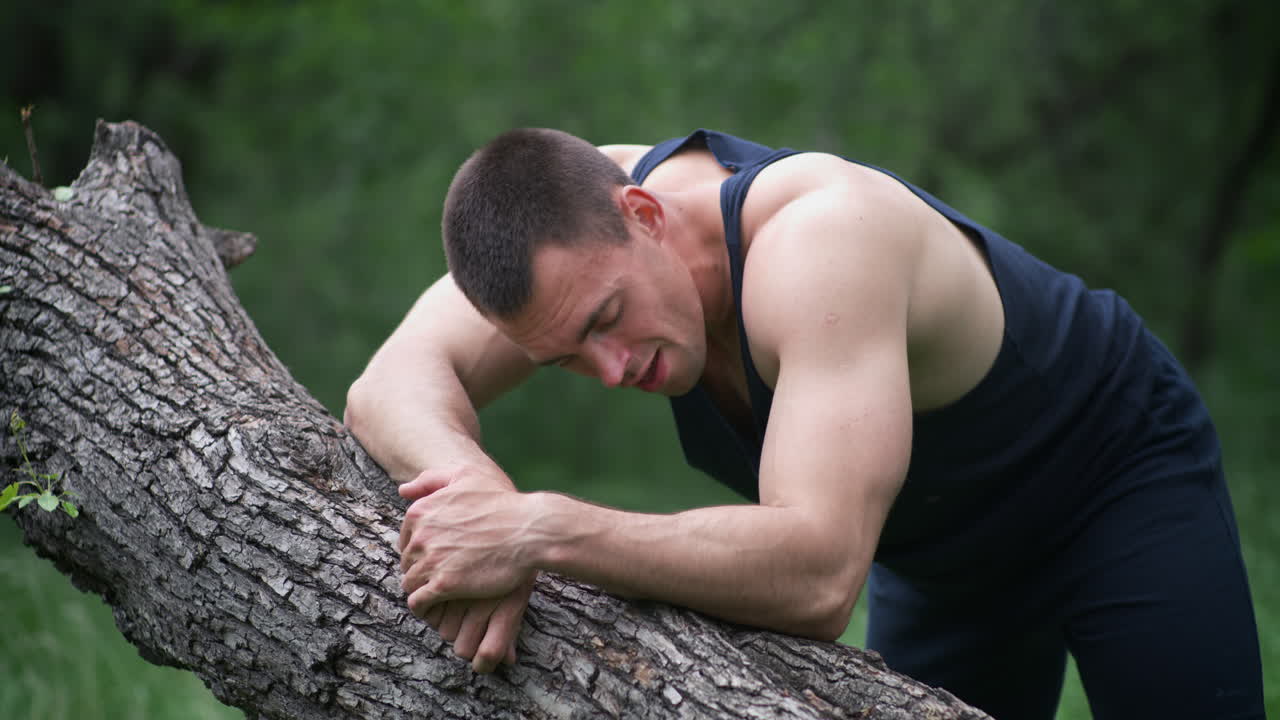 Man resting on a fallen tree trunk during an outdoor workout