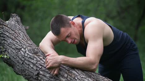 man resting on a fallen tree trunk during an outdoor workout