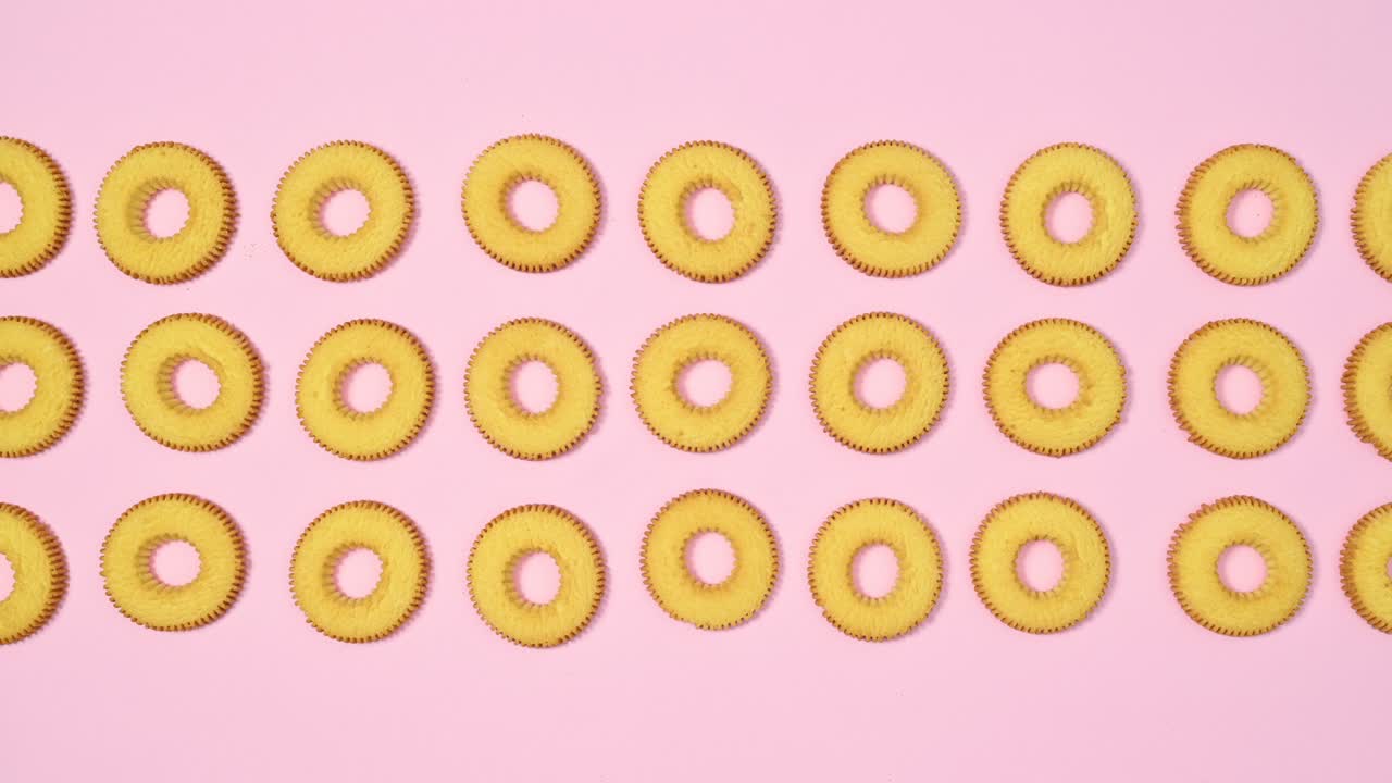 Round cookies biscuits move in three columns on pastel pink theme. Stop motion flat lay