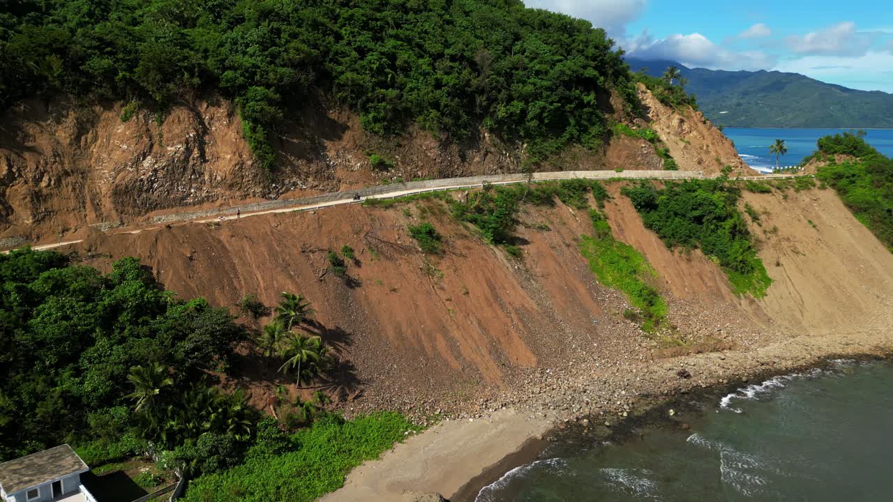 An elevated view of a hillside road in Dingalan, Aurora, winding along vibrant yellow slopes above the coastline, showcasing the dramatic contrast of forested hills and turquoise sea