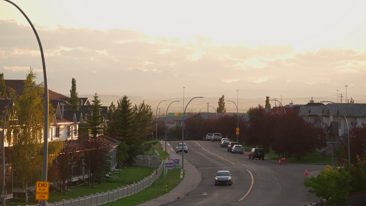 Colorful sunset at golden hour in the city with houses with a road leading into the distance with cars driving.