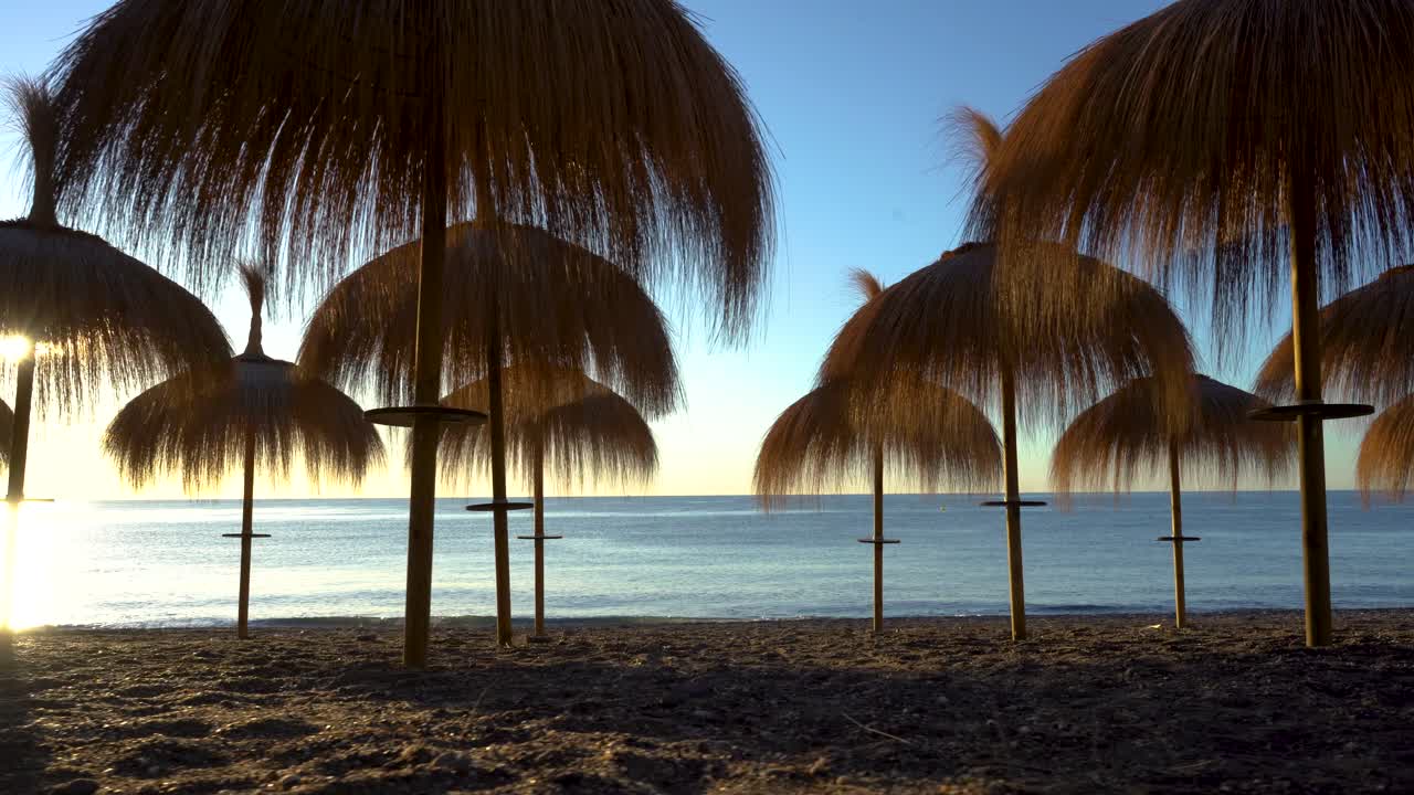 amanecer moviéndose a baja altura de sombrillas de paja en la playa de marbella, vista cinematográfica de cardán de 4k