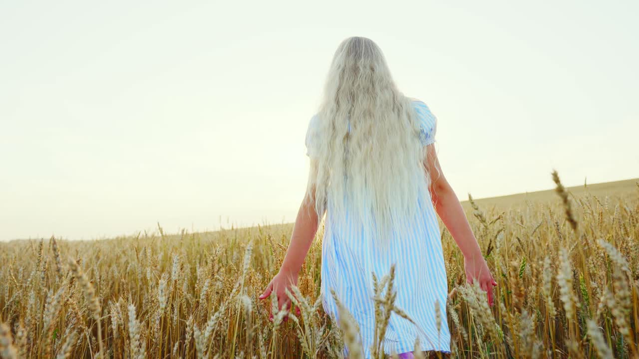 Young Girl with Long Blonde Hair Walking Through Wheat Field at Sunset