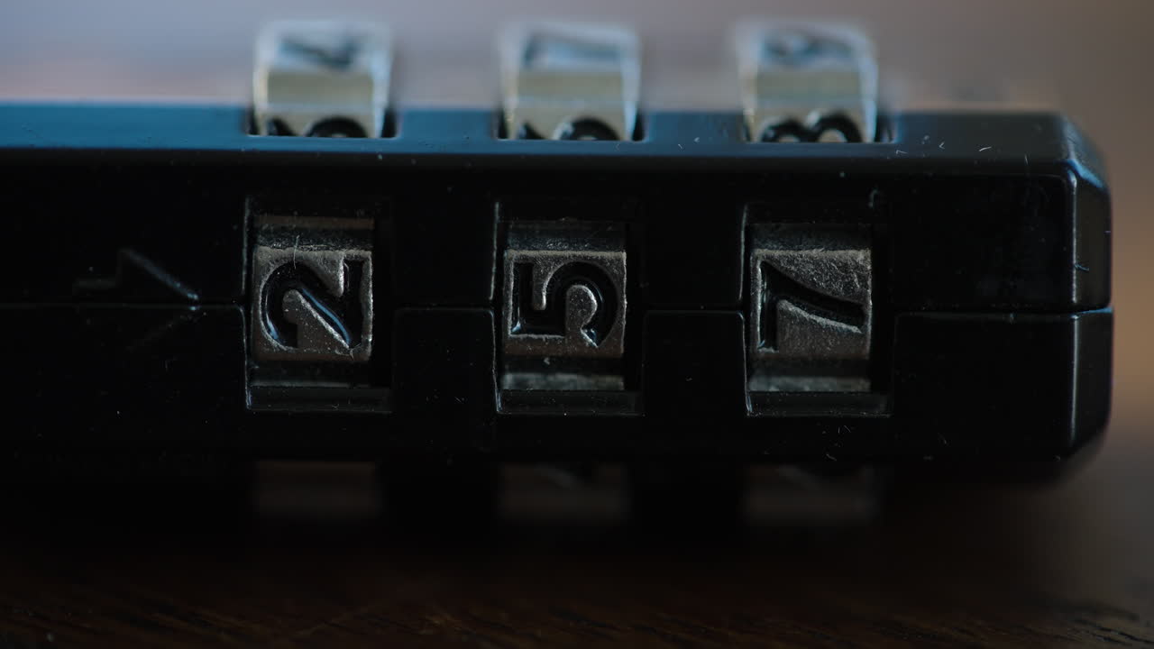 Extreme macro shot of a dusty combination padlock sitting on a wooden table while shadows of people walking by flicker across the surface