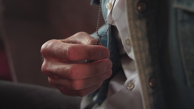 Man holds gothic cross necklace while sitting on a church pew