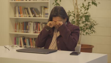 Middle-aged-woman-with-reading-glasses-finishes-working-on-laptop-in-library