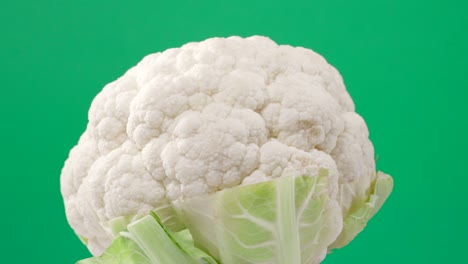 fresh raw cauliflower rotating over green background