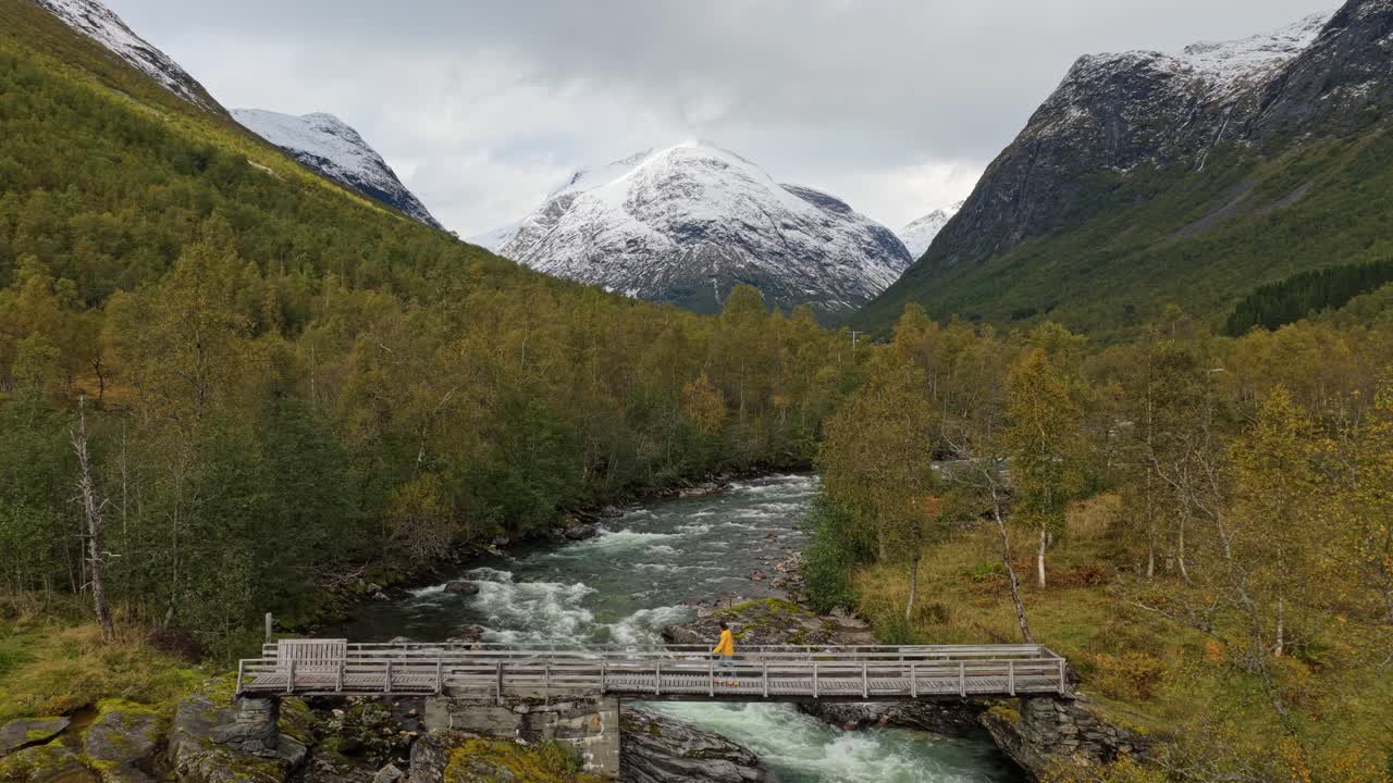 Uomo che attraversa un ponte rustico circondato da montagna e fiume, Norvegia, vista aerea