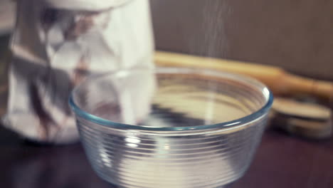 chef sieving powdered sugar for icing in a deep glass bowl. sweet seasoning