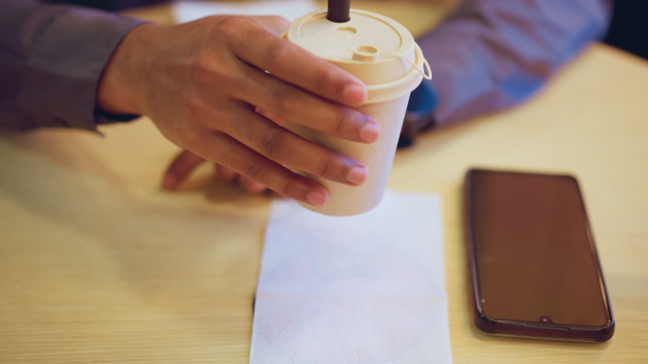 Person in casual shirt wearing smartwatch rests hand on wooden table near smartphone and white tissue napkin in calm indoor environment, suggesting quiet waiting moment or casual relaxed setting in caf