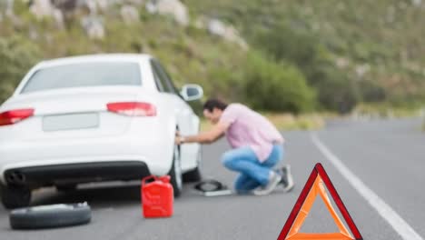 warning triangle in rural road with man kneeling by broken-down white car defocussed in background