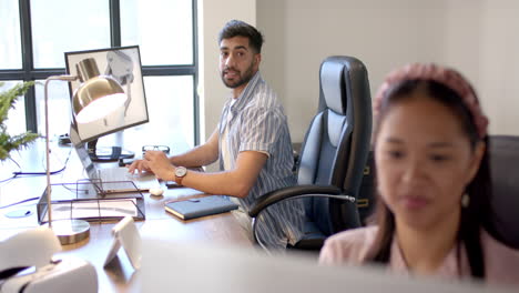 working in office, man using computer and looking back at colleague