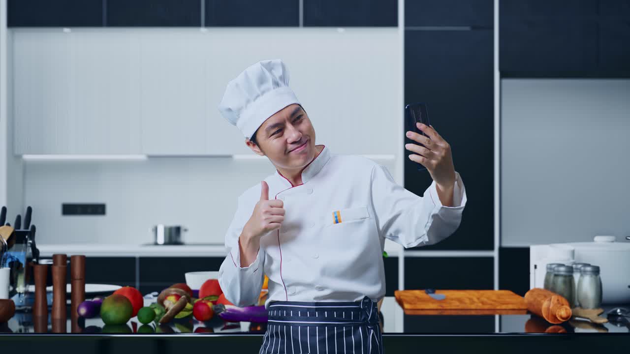 un chef asiático usando un teléfono inteligente tomando fotos mientras está de pie en la cocina de su casa