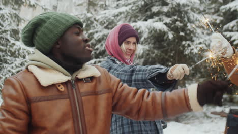 happy friends dancing with christmas sparklers in winter woods