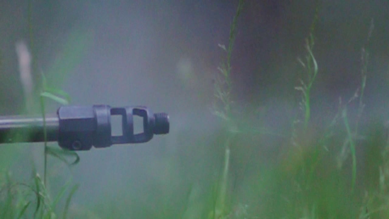 Camouflaged shooter fires precise slow motion shot from grassy woodland position