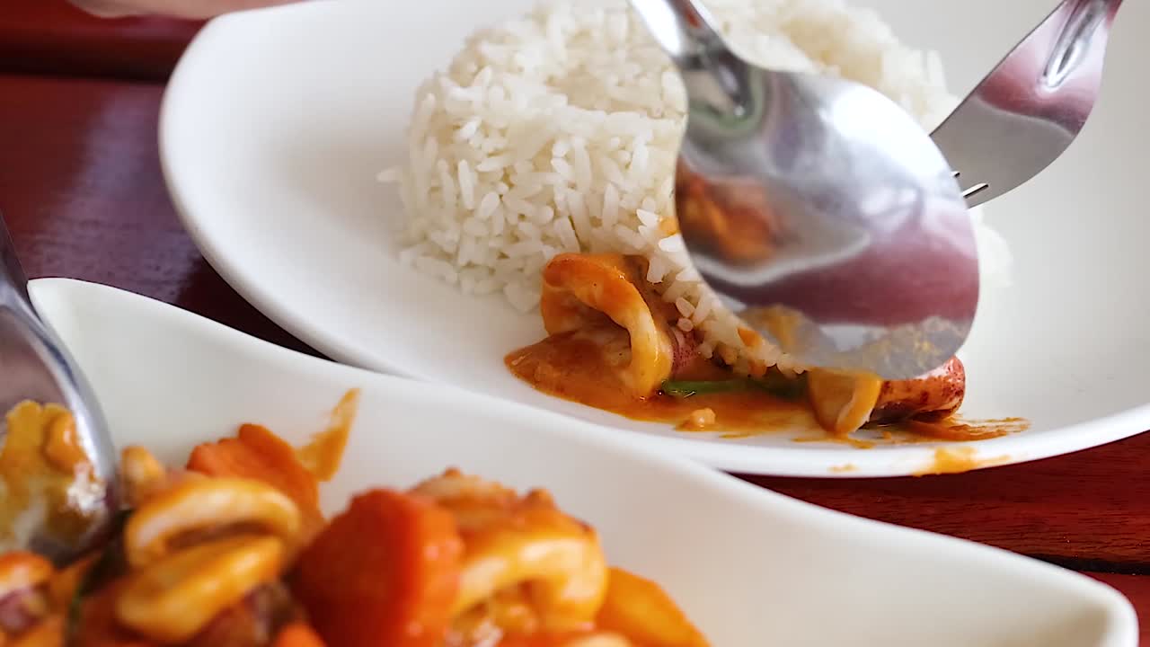 Close-up of stir-fried squid being served with rice using a fork and spoon.
