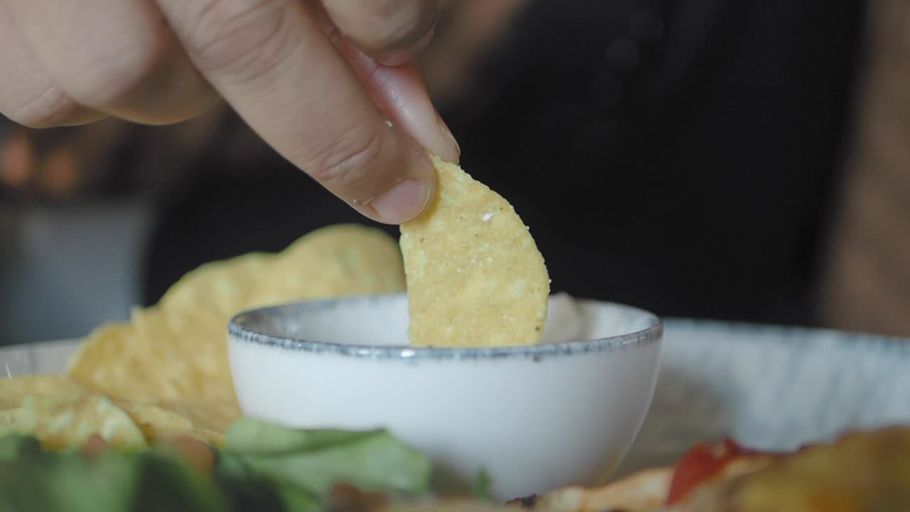 Person dipping tortilla chip in salsa