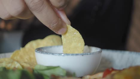 person dipping tortilla chip in salsa