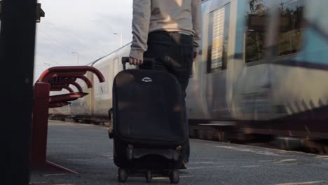 female passenger wheels suitcase on train platform as train goes by wide shot