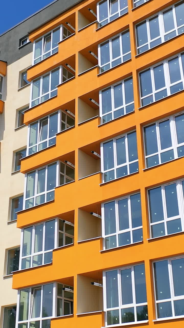 Beautiful high-rise building. Modern block of flats with large balconies on blue sky background in summer. Apartment building of colorful walls. Camera moves down. Vertical video