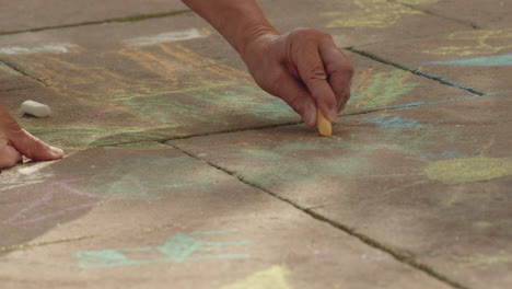 medium shot of the hands of a grandma drawing with an orange piece of chalk onto some stones outside