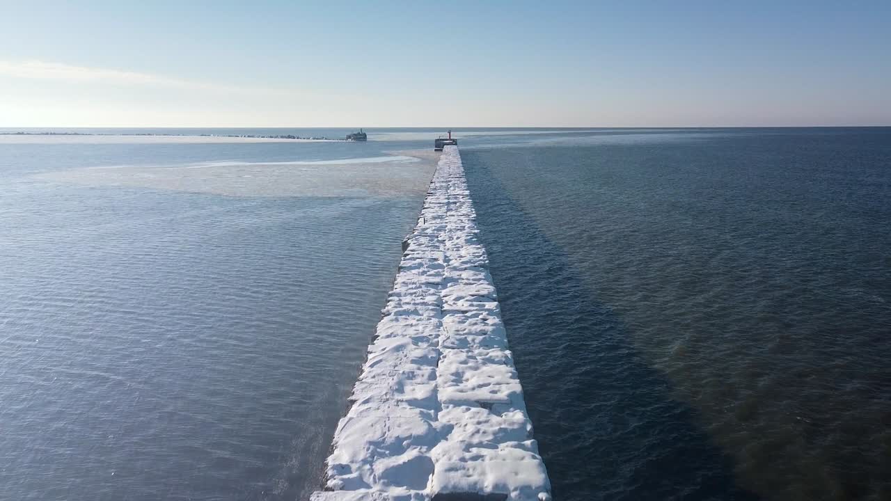 화창한 겨울날 리파자 항구, 잔잔한 발트해의 눈과 얼음으로 덮인 콘크리트 부두의 공중 전망, 앞으로 움직이는 광각 드론 샷 카메라가 천천히 기울어집니다