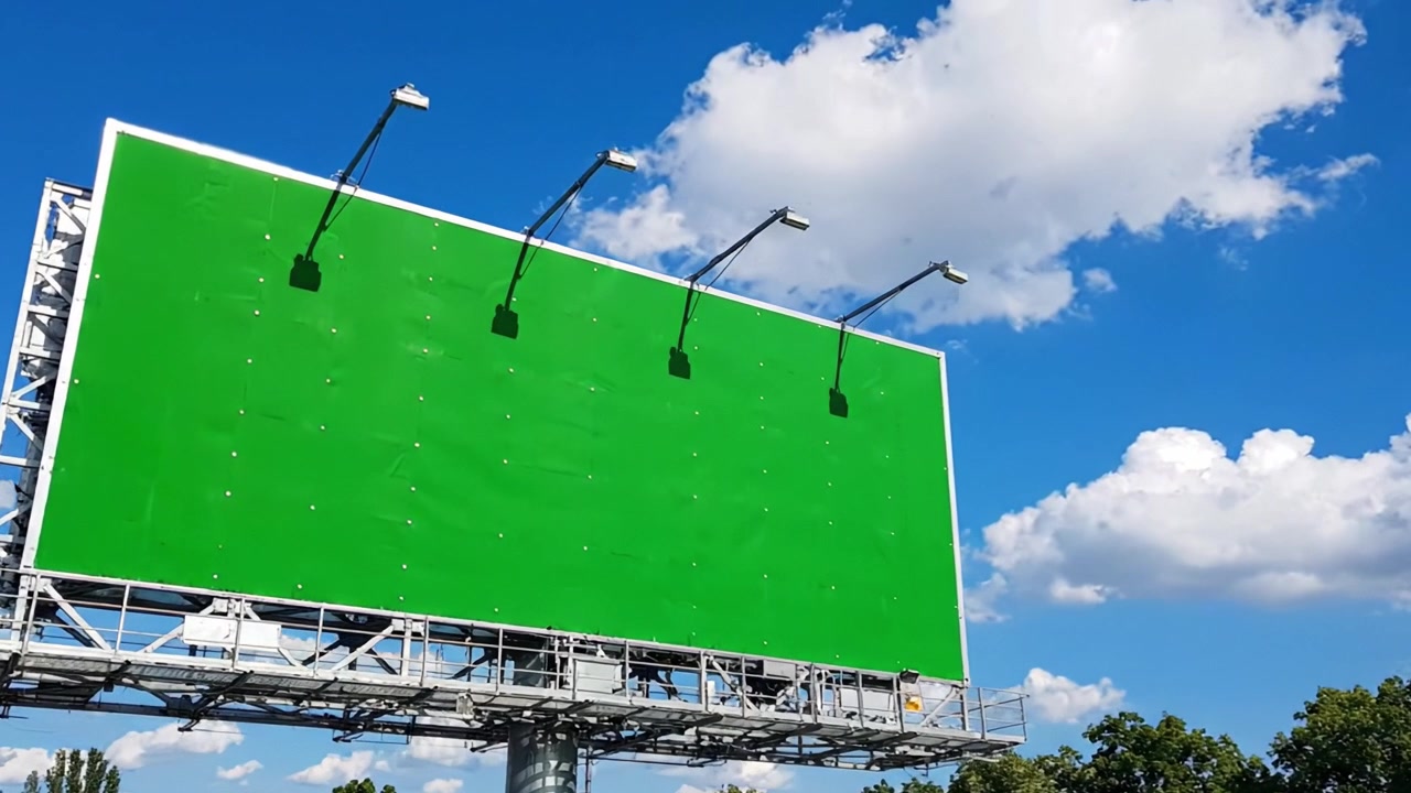 En tom grøn billboard står mod en levende blå himmel fyldt med bløde skyer, hvilket viser en ideel lærred til reklamer eller digitale skærme.