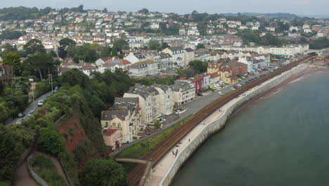 Aufschlussreiche-Luftaufnahme-Der-Stadt-Dawlish-Entlang-Der-Küste-Von-Devon-Mit-Eisenbahnschienen-Und-Gebäuden-Im-Schuss