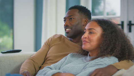 young loving couple hugging and relaxing on sofa at home watching tv together