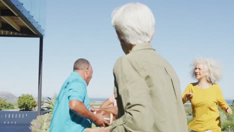 Happy-senior-diverse-people-playing-rugby-in-garden-at-retirement-home