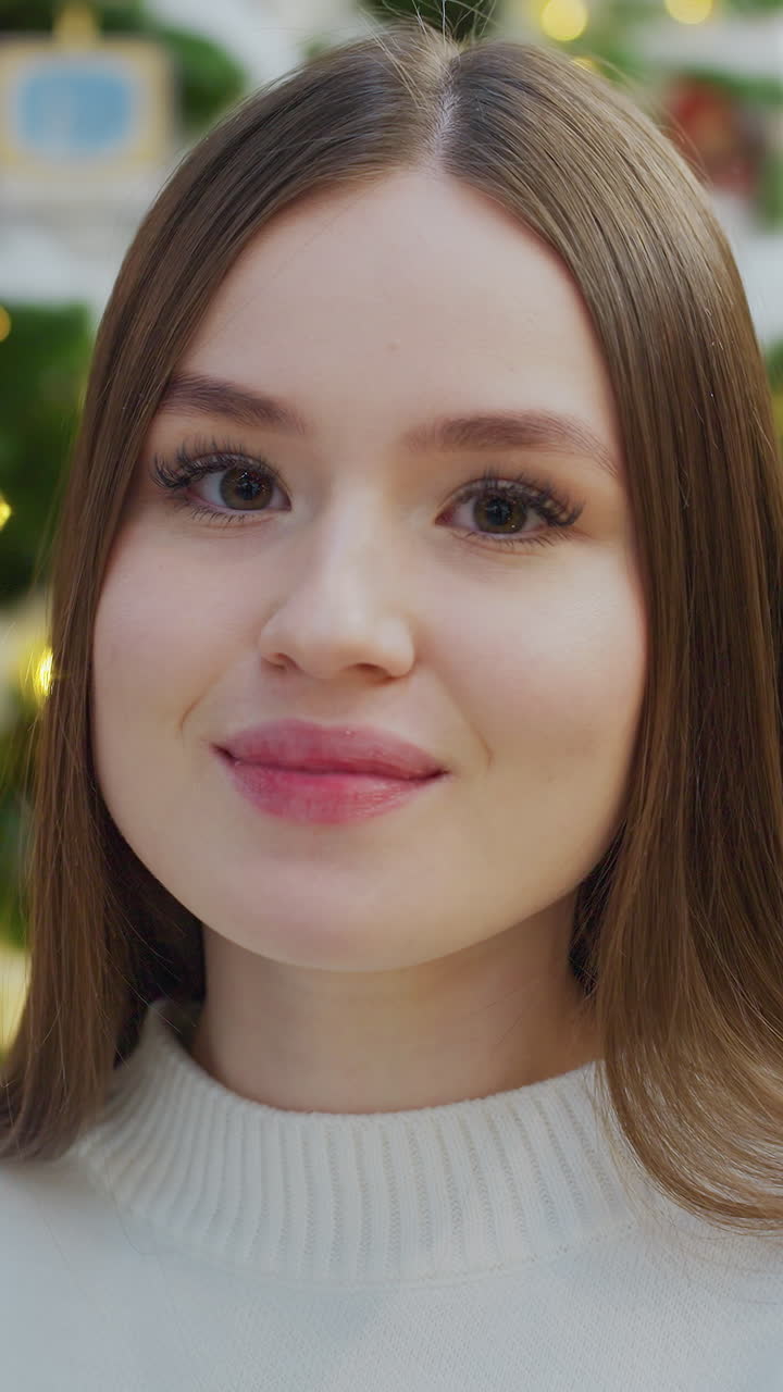 Elegant lady smiling warmly while sitting near beautifully decorated Christmas tree with glowing lights and colorful ornaments, creating a festive and cheerful holiday atmosphere