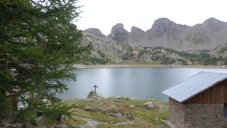 4K-Pan-of-the-Lake-of-Allos-with-Two-Mountain-Cabins-in-the-Foreground,-Alpes-de-Haute-Provence,-France