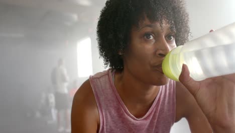 Mujer-Afroamericana-Cansada-Descansando-Y-Bebiendo-Agua-Después-De-Entrenar-En-El-Gimnasio,-En-Cámara-Lenta