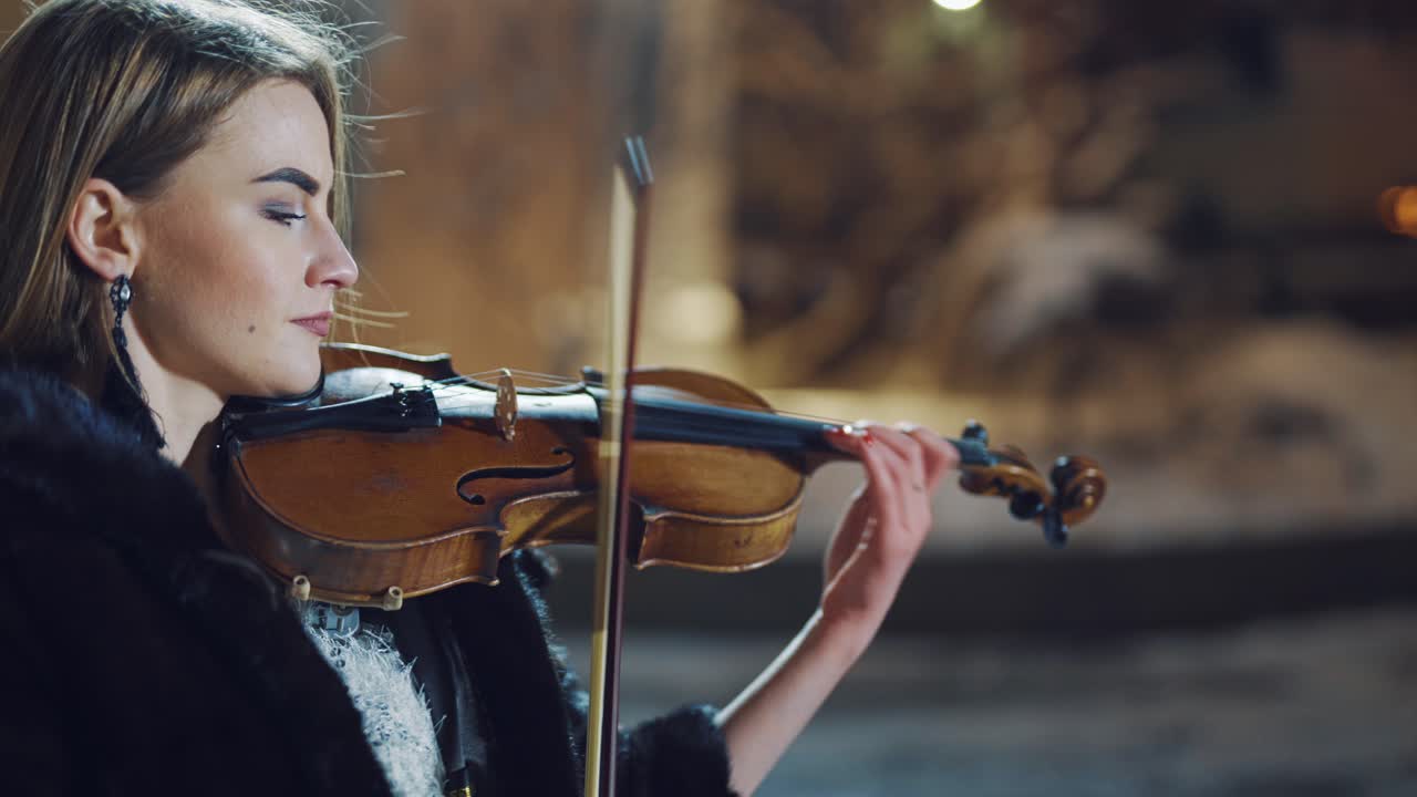 Romantic girl playing on violin at winter park. Female violinist playing classical music on violin at night