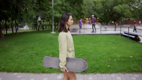 A-girl-walks-in-the-park-with-a-skateboard-in-her-hands,-a-daily-hobby.-Walk-in-the-park,-carry-the-skate-to-the-skateboarders