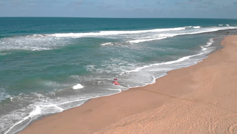 Toma-Aérea-De-Una-Persona-Distante-Saliendo-De-La-Playa-Con-Kayak-Rojo