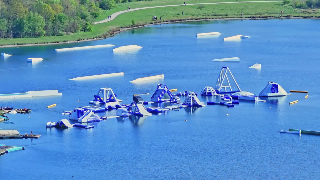 Aerial: aquatic fun park on the lake during the day in Rother Valley Country Park in the Metropolitan Borough of Rotherham, South Yorkshire, England, establishing drone shot