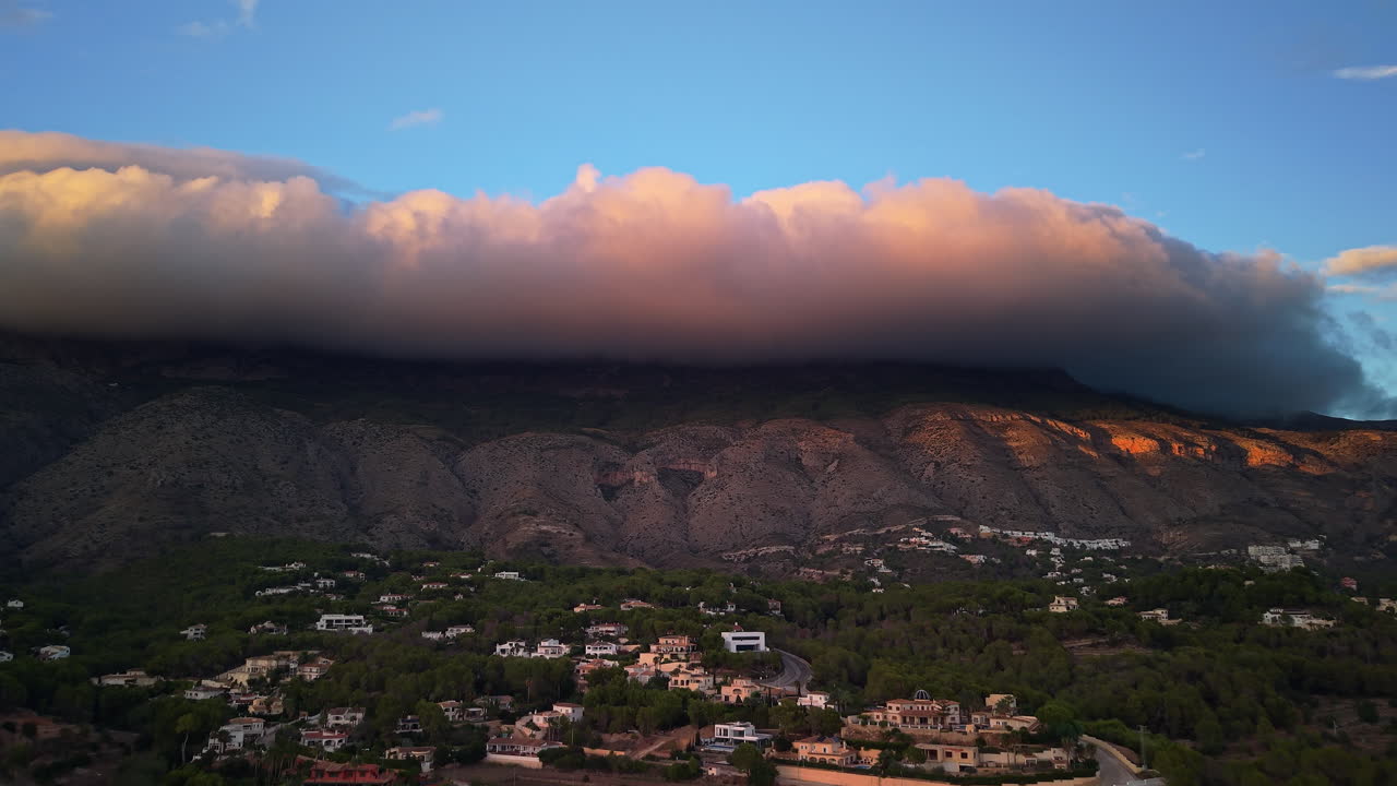 Vista aerea di un villaggio di montagna vicino a Benidorm con nuvole basse e drammatiche e calda luce del tramonto sul paesaggio