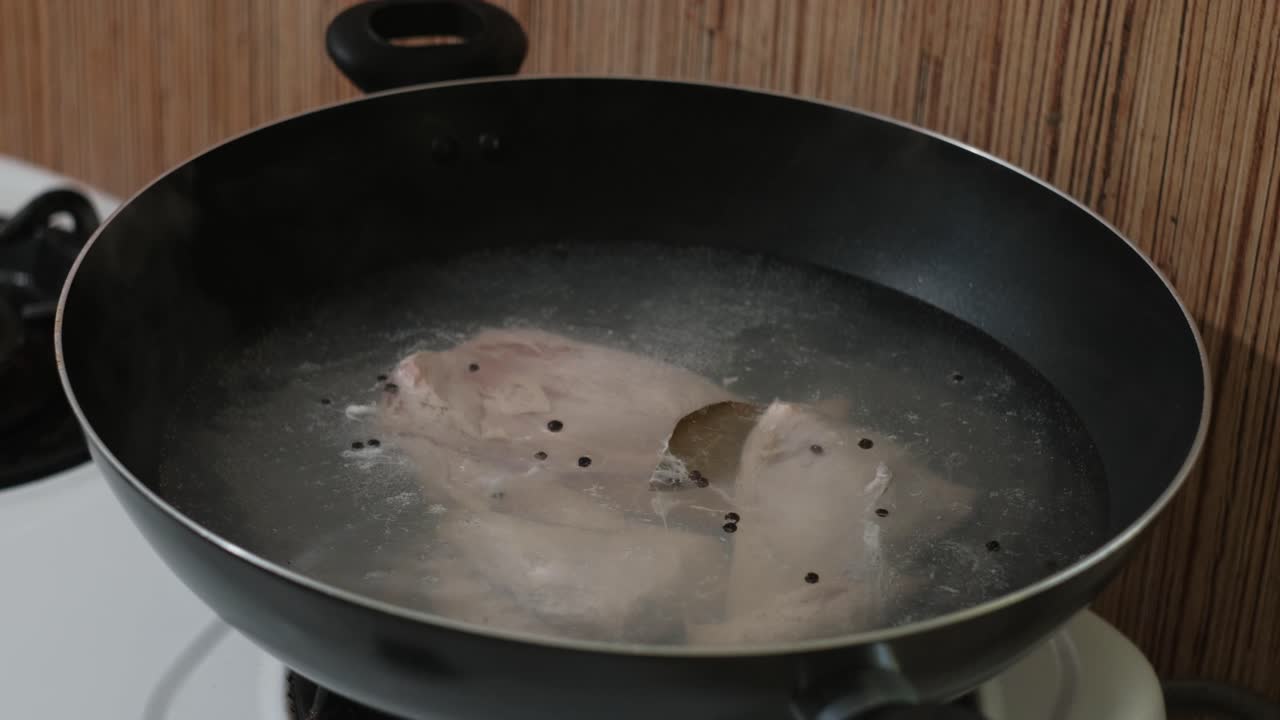 Static shot of chicken parts boiling in wok with seasoning for chicken broth preparation