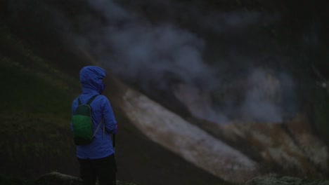 iceland landscape, geothermal hotspring steam smoke, one person watching the smoke rising, camera tilt up, dark and moody evening atmosphere