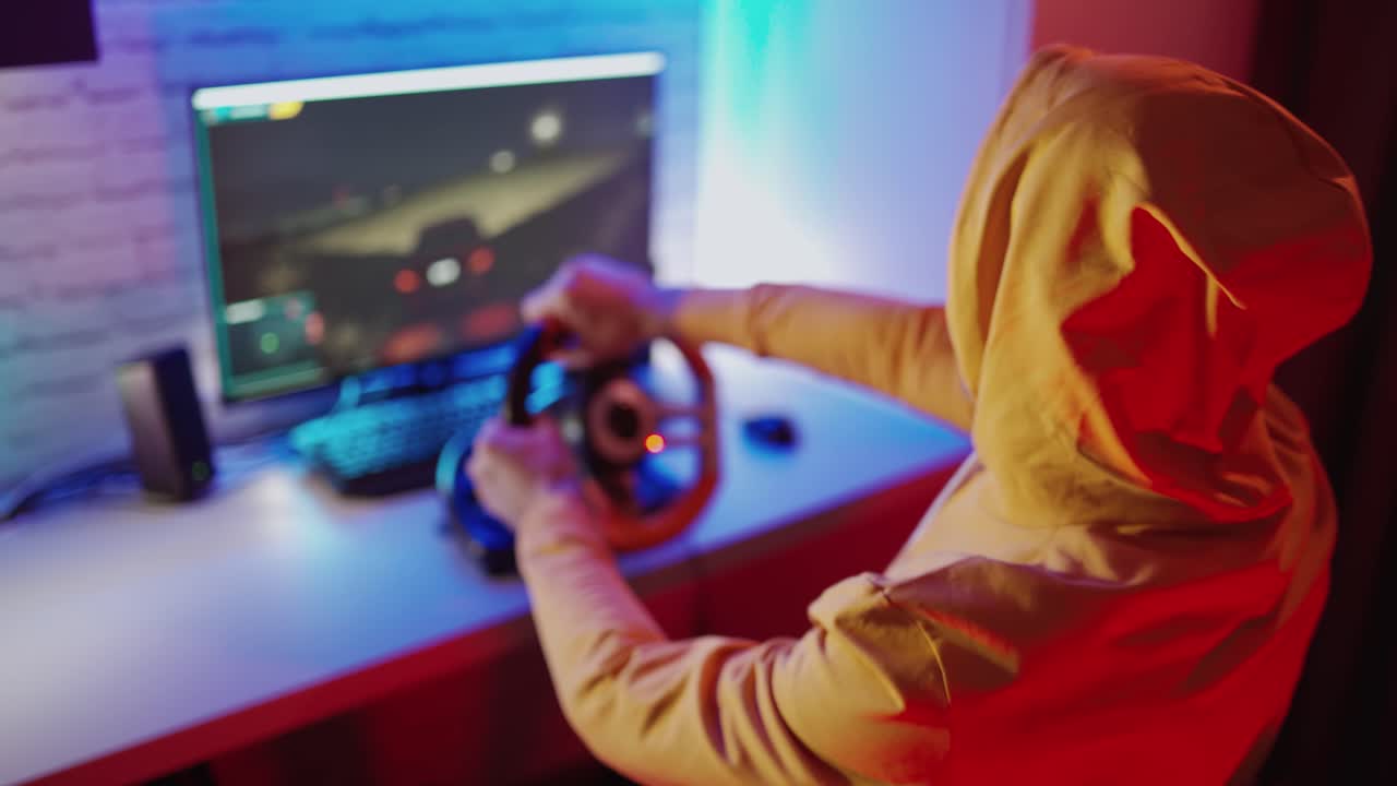 Gamer in orange hood playing video game. Young man enjoys playing car racing with steering wheel at home. Entertainment concept.