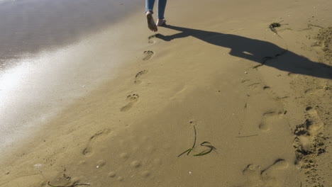 female legs walk along a beach and leave footprints behind