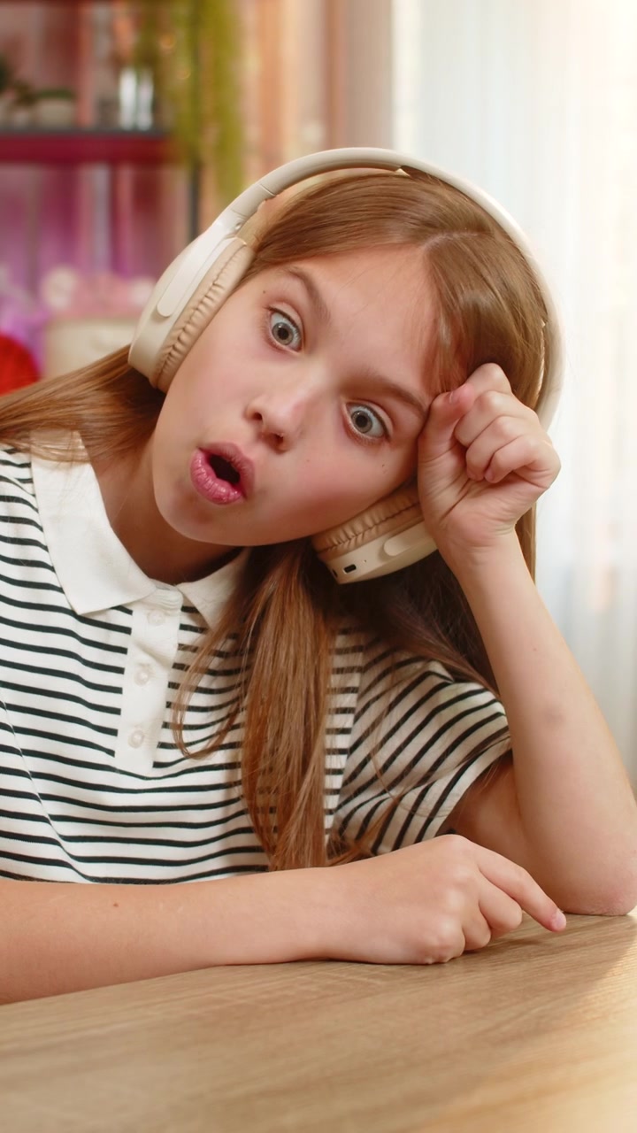 Child girl kid listening to audio fairy tale in headphones at table on home sofa with excitement