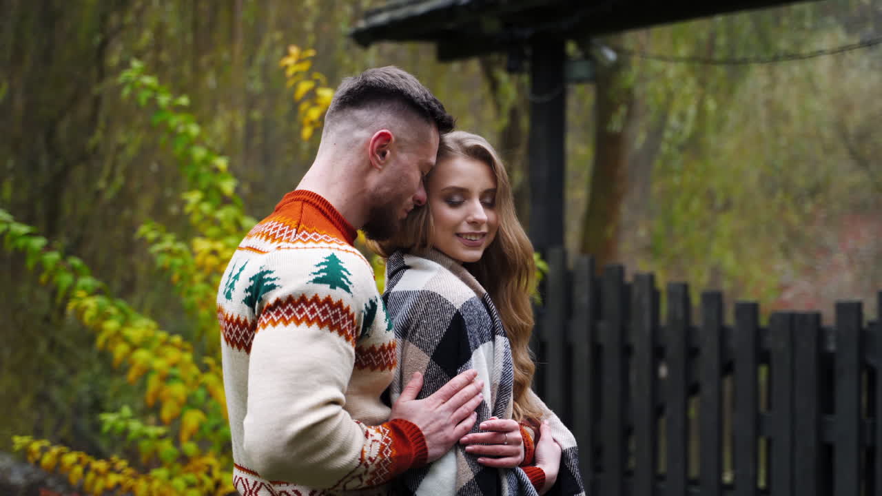 Young man hugged and covered girl with blanket. Beautiful couple outside. Autumn nature background.