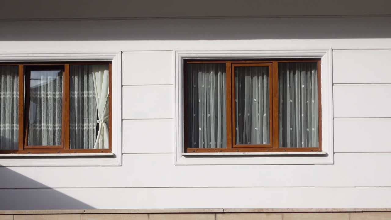 Two windows with curtains on a white wall