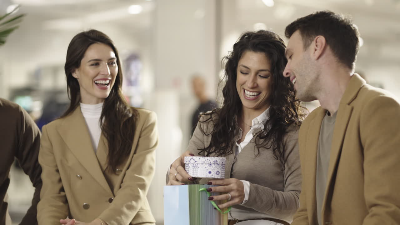 Happy friends or couple opening a gift in a shopping mall