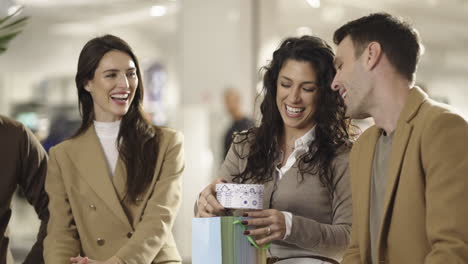 happy friends or couple opening a gift in a shopping mall