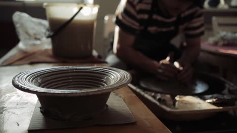 man working on a potter's wheel,and in the foreground there is a ready plate