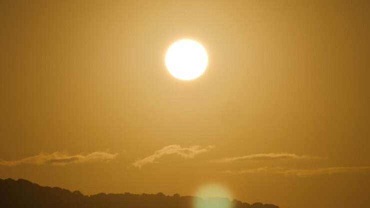 Slow motion shot of golden light and lens flare from shining sun above tiny clouds and hills in Sardinia, Italy
