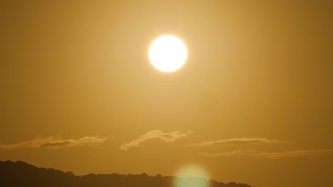 slow motion shot of golden light and lens flare from shining sun above tiny clouds and hills in sardinia, italy